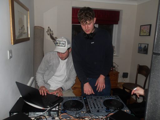 Two young men behind a DJ setup, one using a laptop and the other at the turntables.